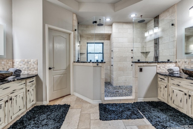 bathroom with stone tile floors, walk in shower, vanity, and decorative backsplash