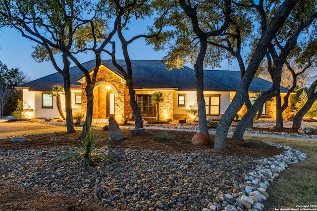 ranch-style home with stone siding, roof with shingles, and stucco siding