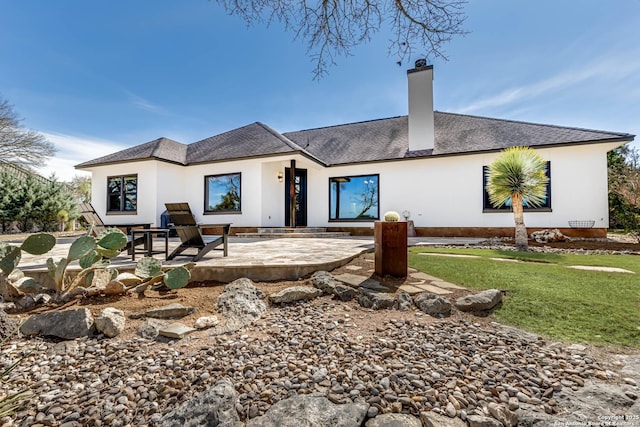 back of property with a yard, a shingled roof, a chimney, and a patio