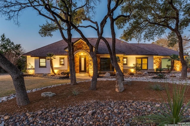 ranch-style house with stone siding, roof with shingles, and stucco siding