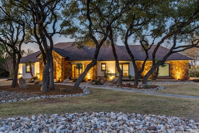 view of front facade with a front yard, stone siding, roof with shingles, and driveway