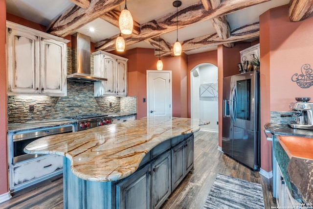 kitchen with arched walkways, dark wood-style flooring, stainless steel appliances, backsplash, and wall chimney exhaust hood