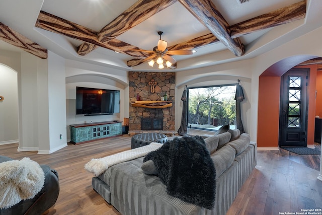 living room with arched walkways, a stone fireplace, coffered ceiling, and wood finished floors