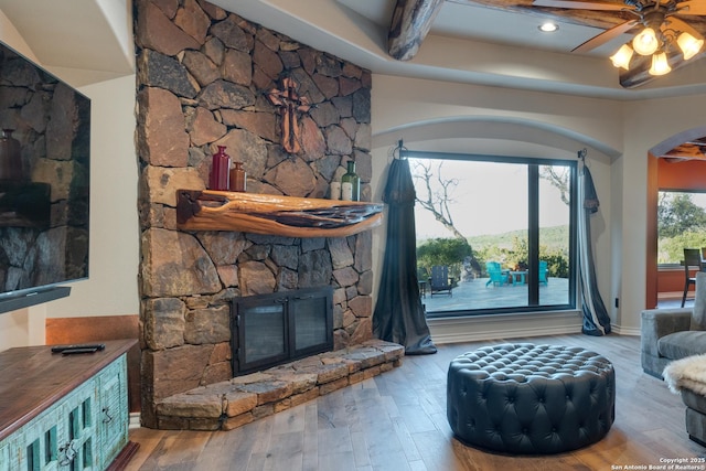 living area with arched walkways, a fireplace, wood finished floors, a ceiling fan, and beamed ceiling