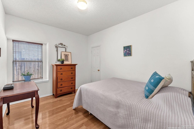 bedroom with light wood finished floors, baseboards, and a textured ceiling