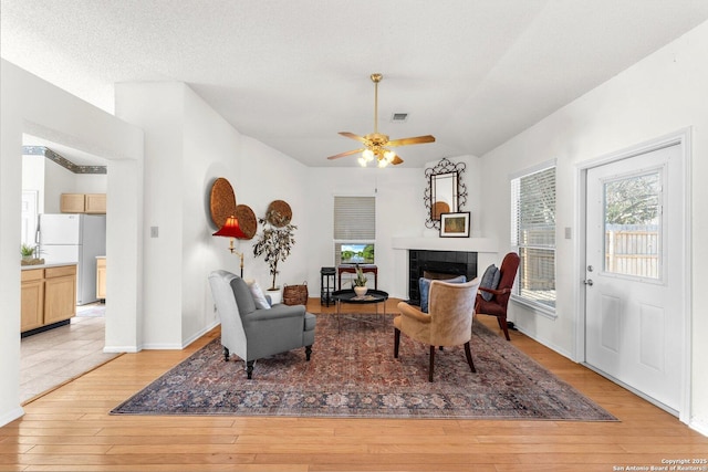 living area featuring light wood-style floors, visible vents, a textured ceiling, and a tile fireplace