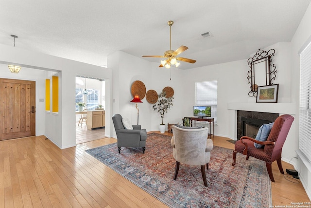 living room with light wood-style flooring, a ceiling fan, visible vents, baseboards, and a tiled fireplace