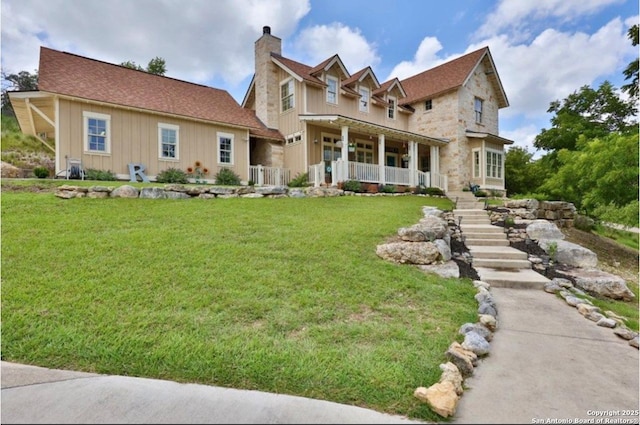 view of front facade with covered porch, stairs, board and batten siding, a front lawn, and a chimney