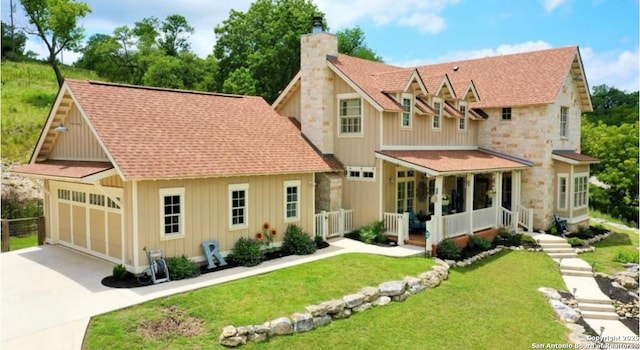 view of front of house with a chimney, covered porch, a garage, driveway, and a front lawn