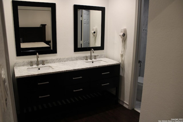 bathroom with a textured wall, double vanity, a sink, and toilet