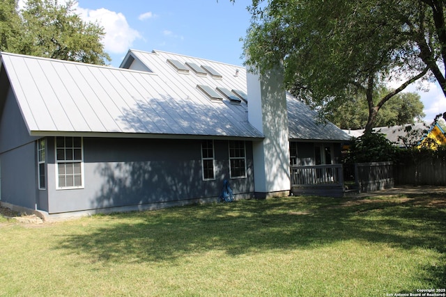 back of house with a standing seam roof, a chimney, metal roof, and a lawn