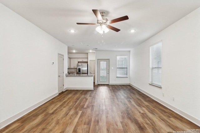 unfurnished living room featuring a healthy amount of sunlight, dark wood-style flooring, a sink, and baseboards