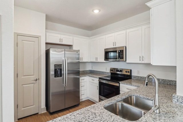 kitchen featuring stainless steel appliances, white cabinetry, a sink, and light stone countertops
