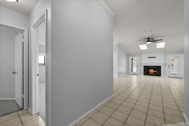 interior space with crown molding, light tile patterned floors, ceiling fan, a tile fireplace, and baseboards