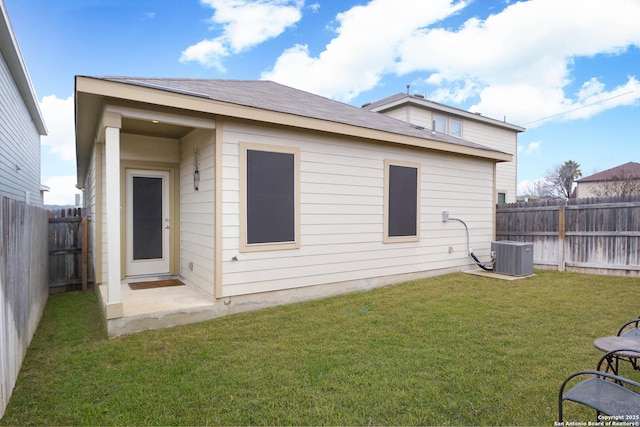 back of property with central air condition unit, a fenced backyard, and a lawn