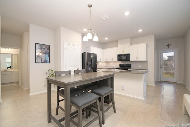 kitchen with decorative light fixtures, recessed lighting, a kitchen island with sink, white cabinetry, and black appliances