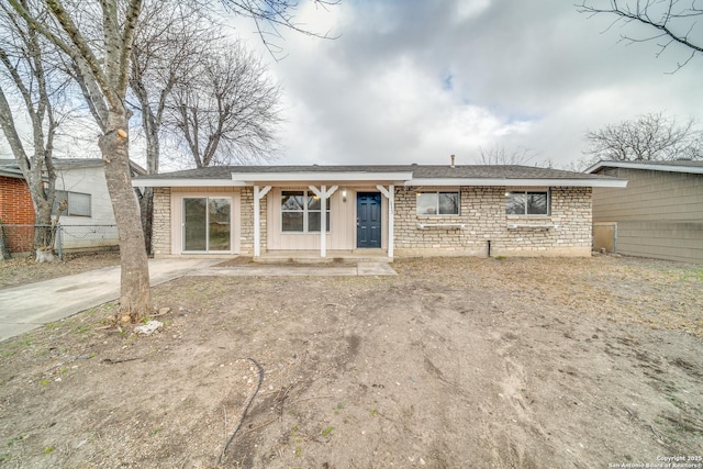 view of front of home with stone siding, a shingled roof, and fence