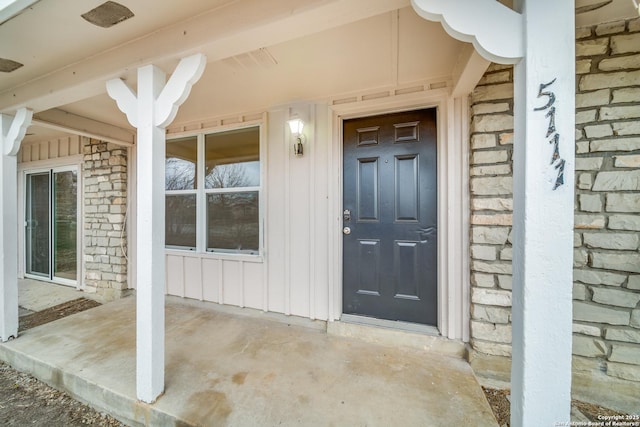 entrance to property with stone siding, covered porch, and board and batten siding