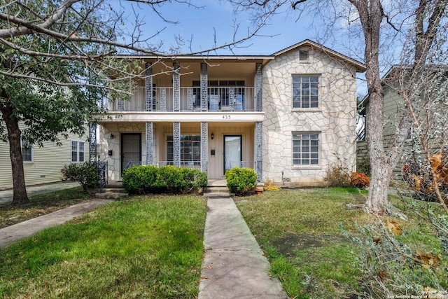 view of front facade with stone siding, a porch, a front yard, and a balcony