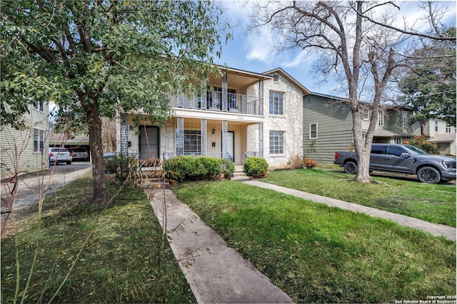 view of front of house with a front yard, stone siding, covered porch, and a balcony