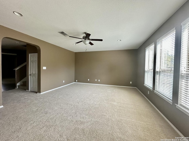 spare room featuring arched walkways, light colored carpet, a textured ceiling, baseboards, and stairs