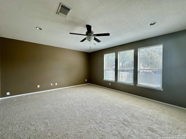 carpeted empty room with a textured ceiling, a ceiling fan, visible vents, and baseboards