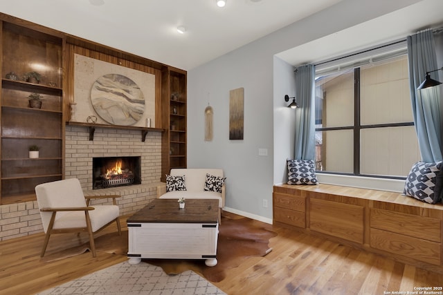 sitting room featuring built in shelves, a brick fireplace, wood finished floors, and baseboards