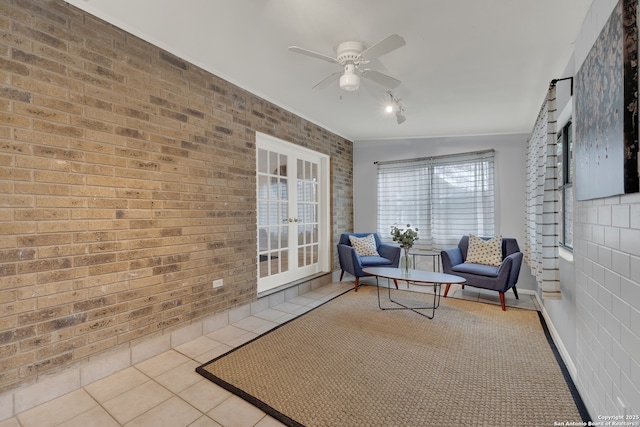 living area with tile patterned flooring, french doors, ceiling fan, and brick wall