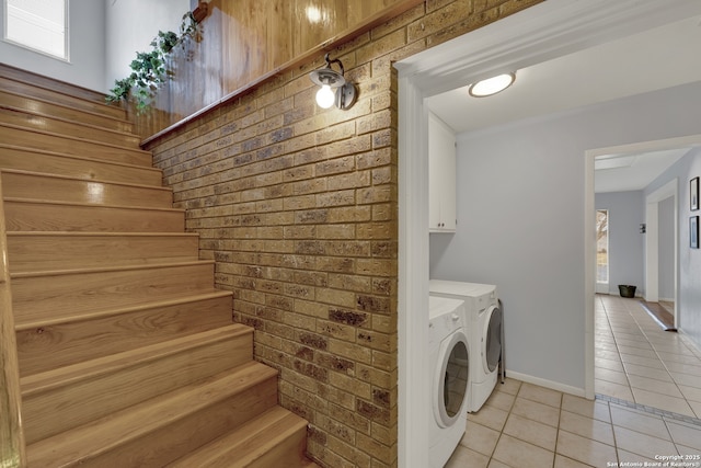 washroom with light tile patterned floors, brick wall, baseboards, independent washer and dryer, and cabinet space