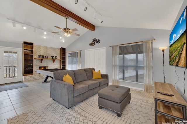 living area featuring a ceiling fan, a brick fireplace, vaulted ceiling with beams, and light tile patterned floors