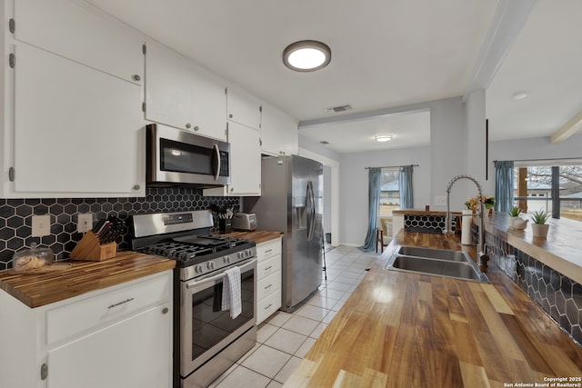 kitchen featuring stainless steel appliances, a sink, visible vents, wooden counters, and decorative backsplash