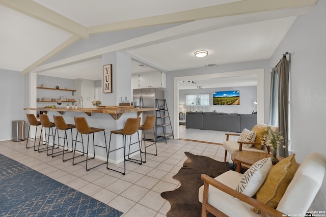 interior space with baseboards, visible vents, stainless steel fridge with ice dispenser, vaulted ceiling with beams, and light tile patterned flooring