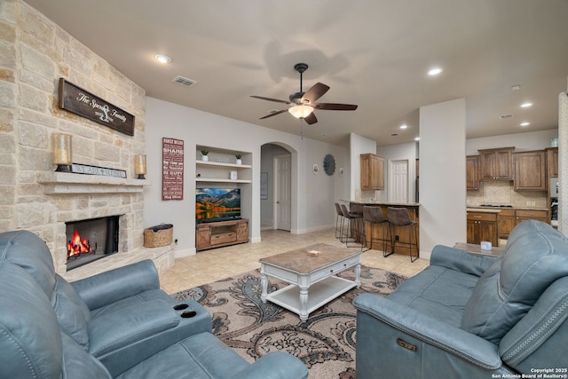 living area featuring arched walkways, a fireplace, visible vents, light tile patterned flooring, and baseboards