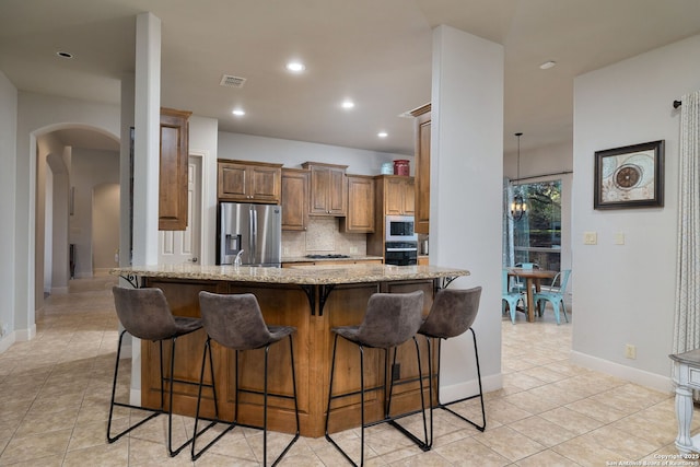 kitchen featuring arched walkways, a breakfast bar area, visible vents, black oven, and stainless steel fridge