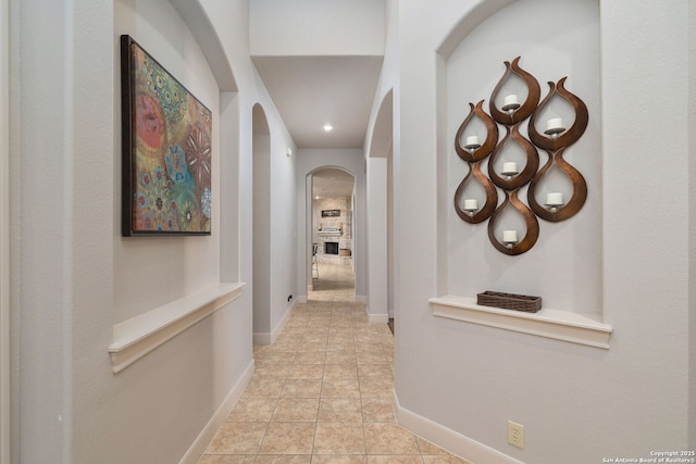 corridor with light tile patterned floors, baseboards, and arched walkways