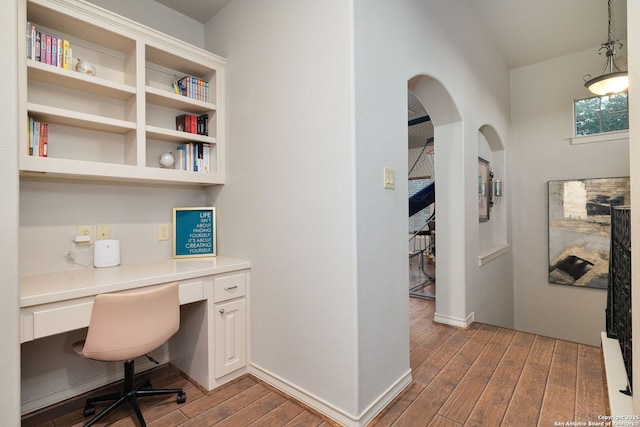 office space with baseboards, arched walkways, built in desk, and wood finished floors