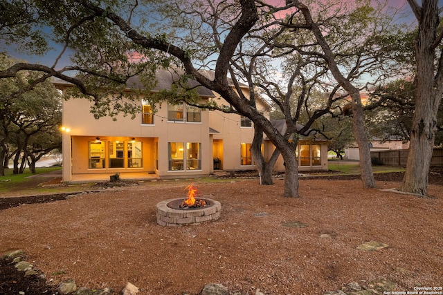 back of house at dusk featuring an outdoor fire pit and stucco siding