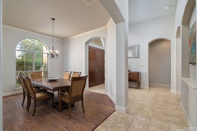 dining area featuring arched walkways, light wood-style flooring, a notable chandelier, baseboards, and crown molding