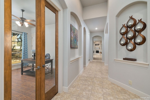 corridor featuring light tile patterned floors, arched walkways, and baseboards