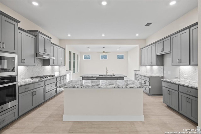 kitchen with light stone counters, stainless steel appliances, a sink, a kitchen island, and under cabinet range hood