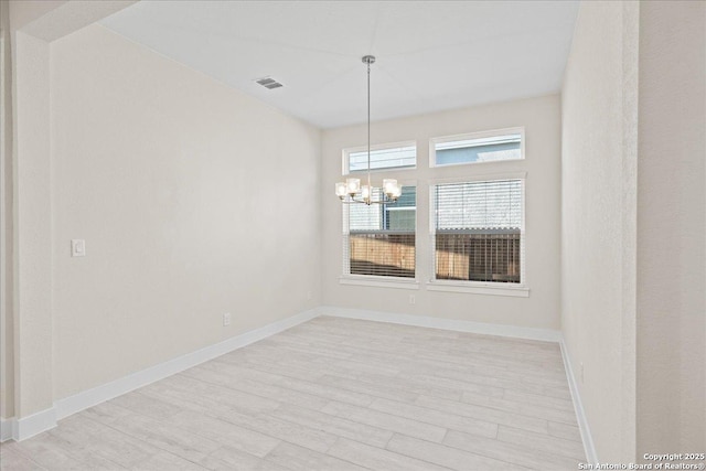 empty room featuring baseboards, light wood-style flooring, visible vents, and a notable chandelier