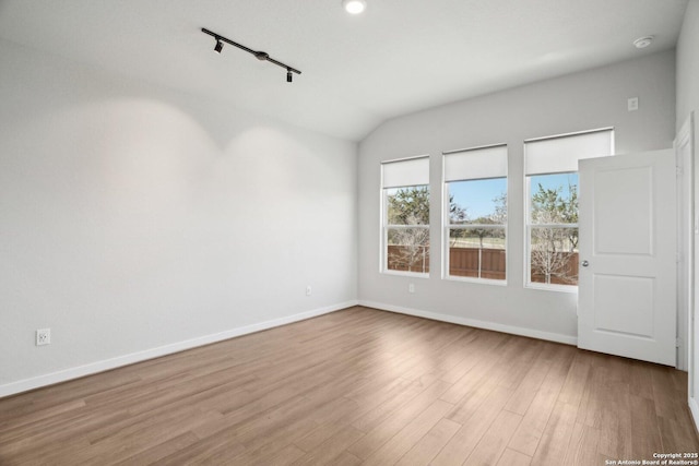 empty room with rail lighting, baseboards, vaulted ceiling, and wood finished floors