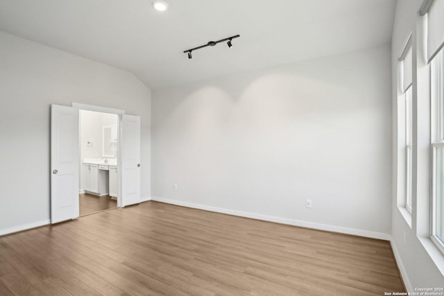 unfurnished bedroom featuring light wood-type flooring, multiple windows, baseboards, and lofted ceiling