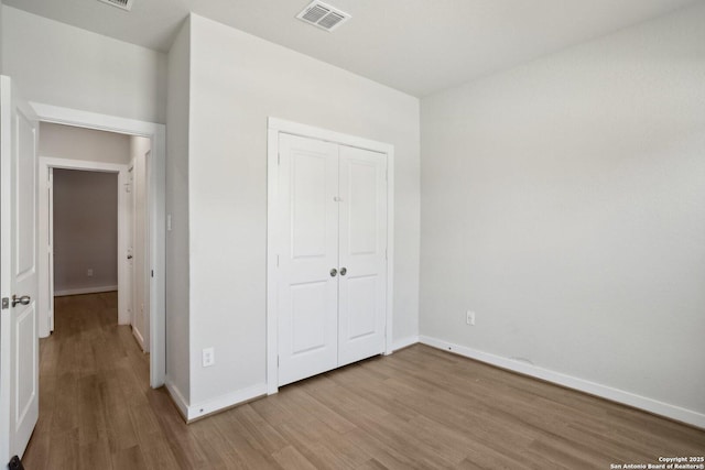 unfurnished bedroom with a closet, visible vents, baseboards, and wood finished floors