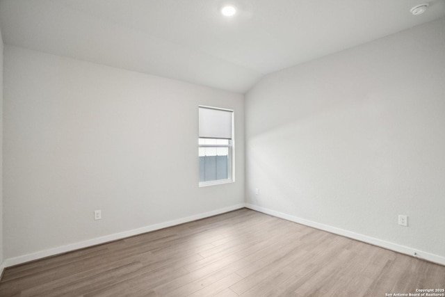 spare room featuring lofted ceiling, wood finished floors, and baseboards