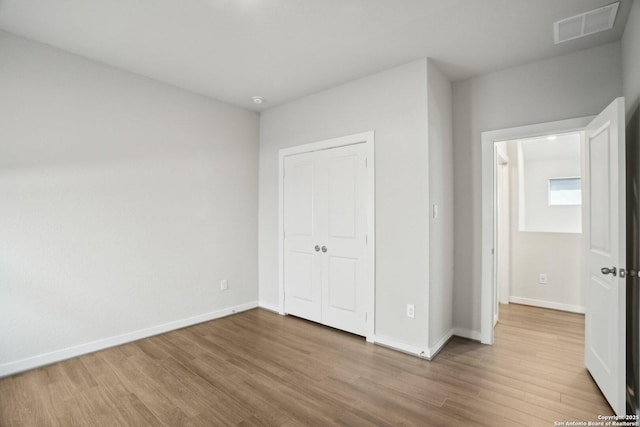 unfurnished bedroom featuring baseboards, a closet, visible vents, and wood finished floors