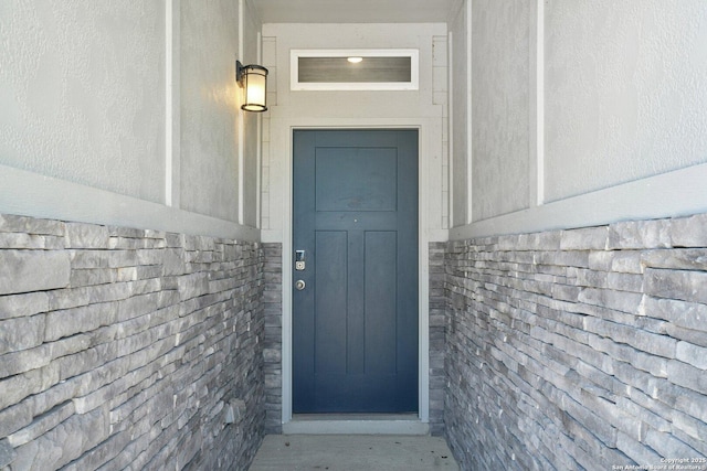 property entrance with stone siding, roof with shingles, and stucco siding