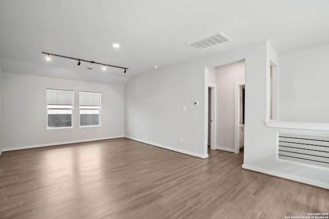 empty room featuring track lighting, wood finished floors, visible vents, and baseboards