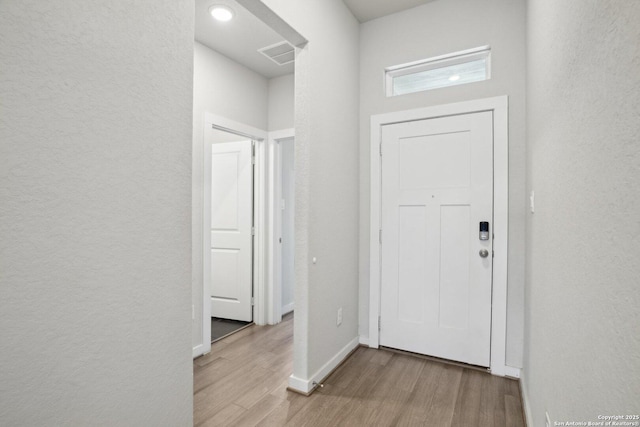 interior space featuring visible vents, a textured wall, baseboards, and wood finished floors