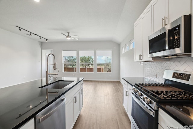 kitchen featuring dark countertops, decorative backsplash, appliances with stainless steel finishes, white cabinetry, and a sink